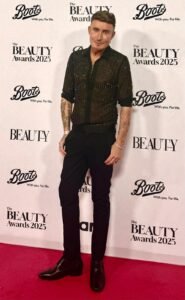 Full length photo of TJ Shirley from TJtutorials in a black embellished PHIX shirt and Gucci trousers in front of The Beauty Awards Official 2025 backdrop.