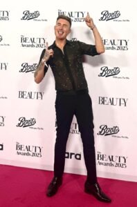 TJ Shirley smiling and pointing towards The Beauty Awards 2025 logo on the red carpet.